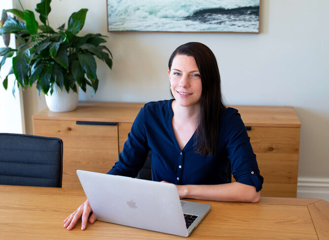 Minja sitting a table with her laptop smiling